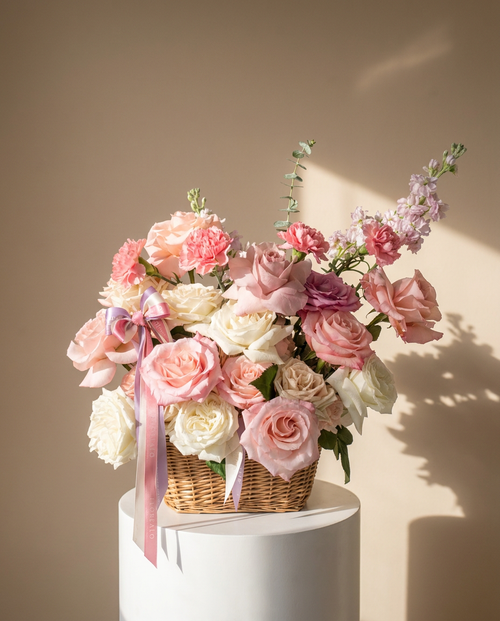 Bouquet of pink and white flowers with a pink ribbon in a wicker basket on a beige background